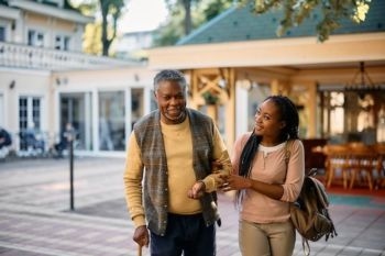 Smiling woman assisting elderly man with cane outdoors, symbolizing how a living trust helps protect assets and ensure smooth transfer of wealth to loved ones.